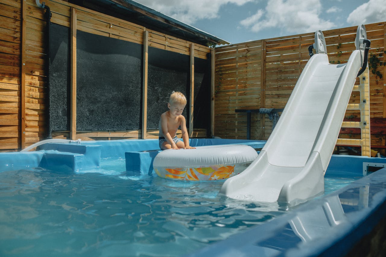 Services Young child playing with inflatable in a pool with slide during summer.