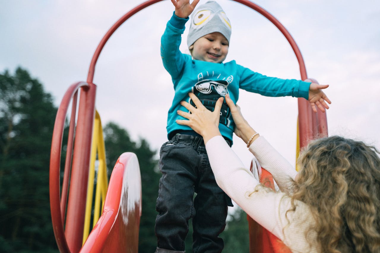 Home A joyful moment of a mother catching her child at the top of a playground slide.