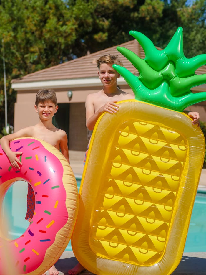 Two boys having fun with inflatable rings at a poolside on a sunny summer day.